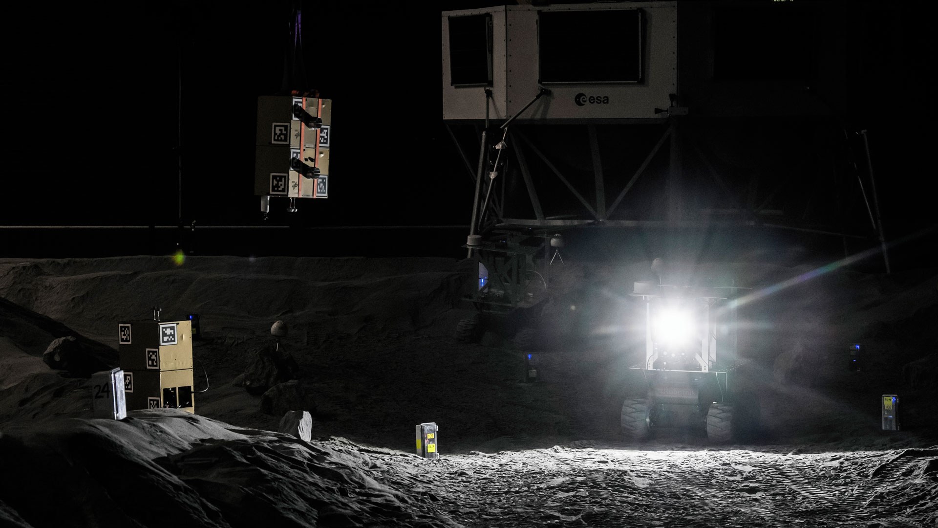 Das Bild zeigt einen Rover vor einem Lander in der dunklen LUNA-Halle.