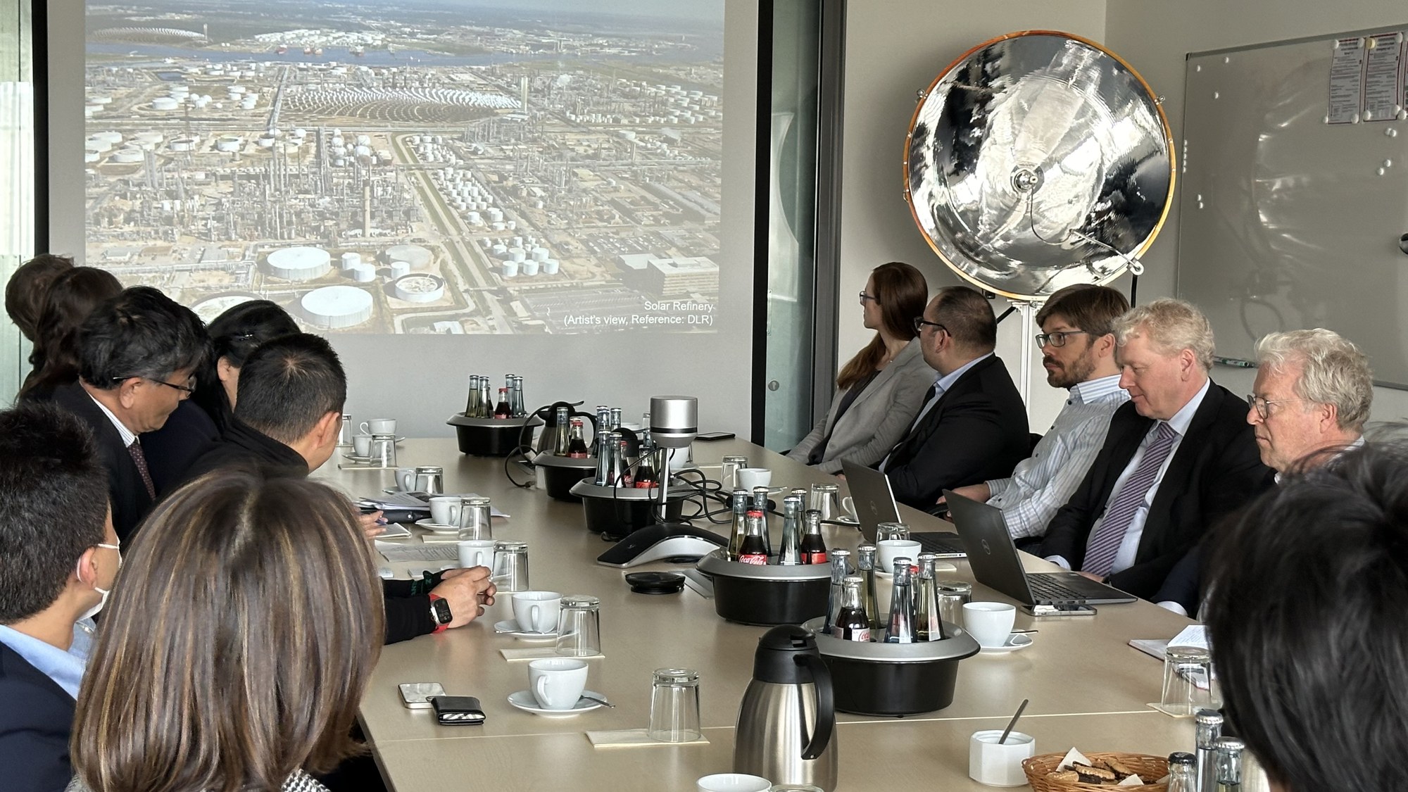 Die Wirtschafts-Delegation aus Fukushima sitzt während einer Präsentation im Synlight gegenüber Mitarbeitenden des DLR ein einem Sitzungsraum.