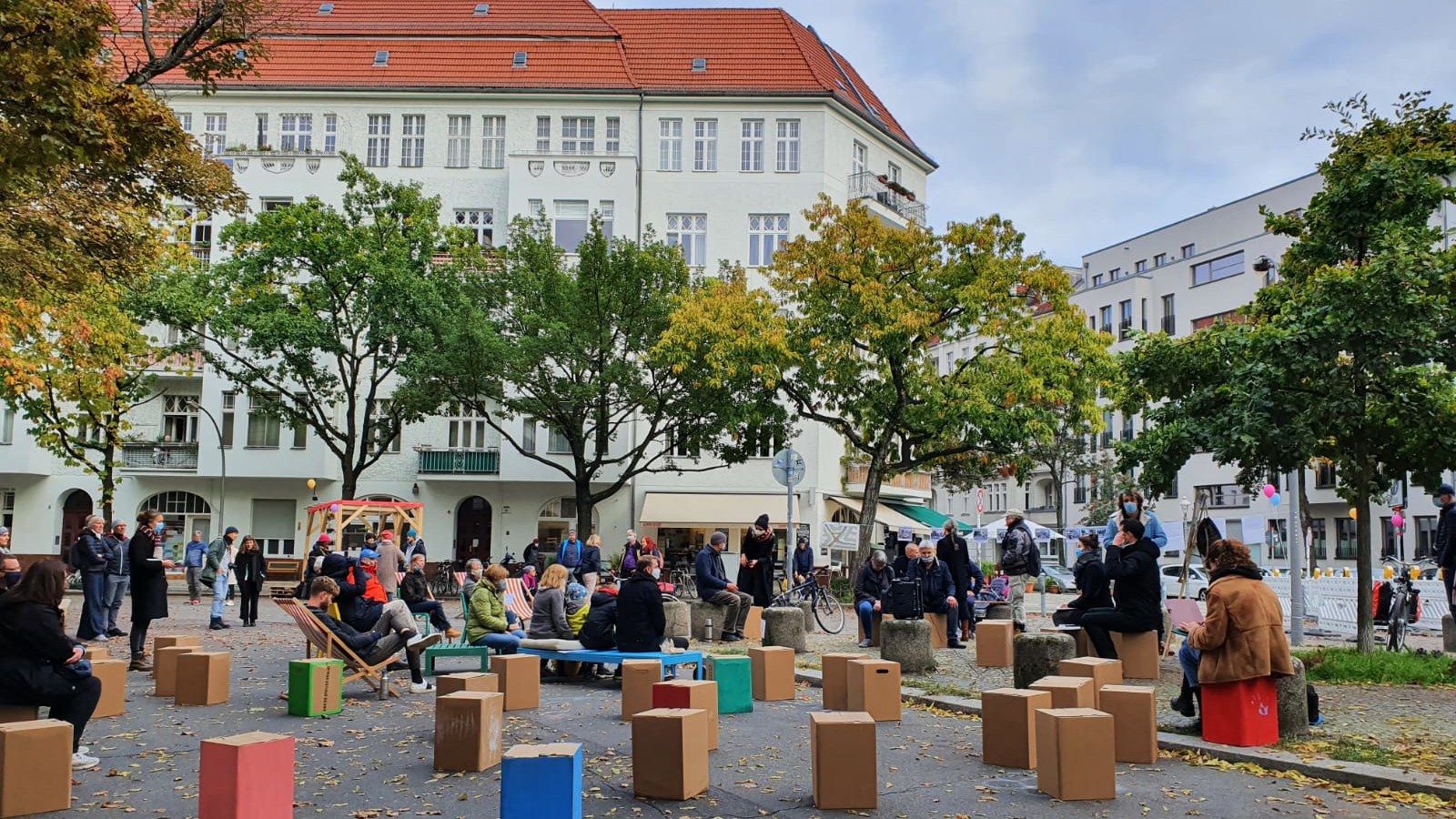 Ein Bild eines Stadtplatzes, der umfunktioniert wurde. Auf der Straße stehen Papp-Hocker in bunten Farben.