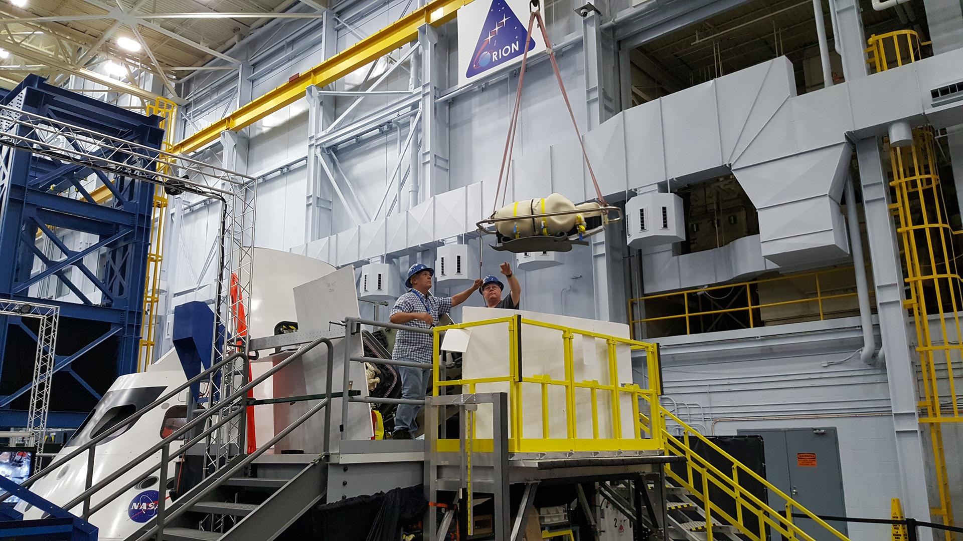 Replica phantom lifted above the Orion capsule by a crane