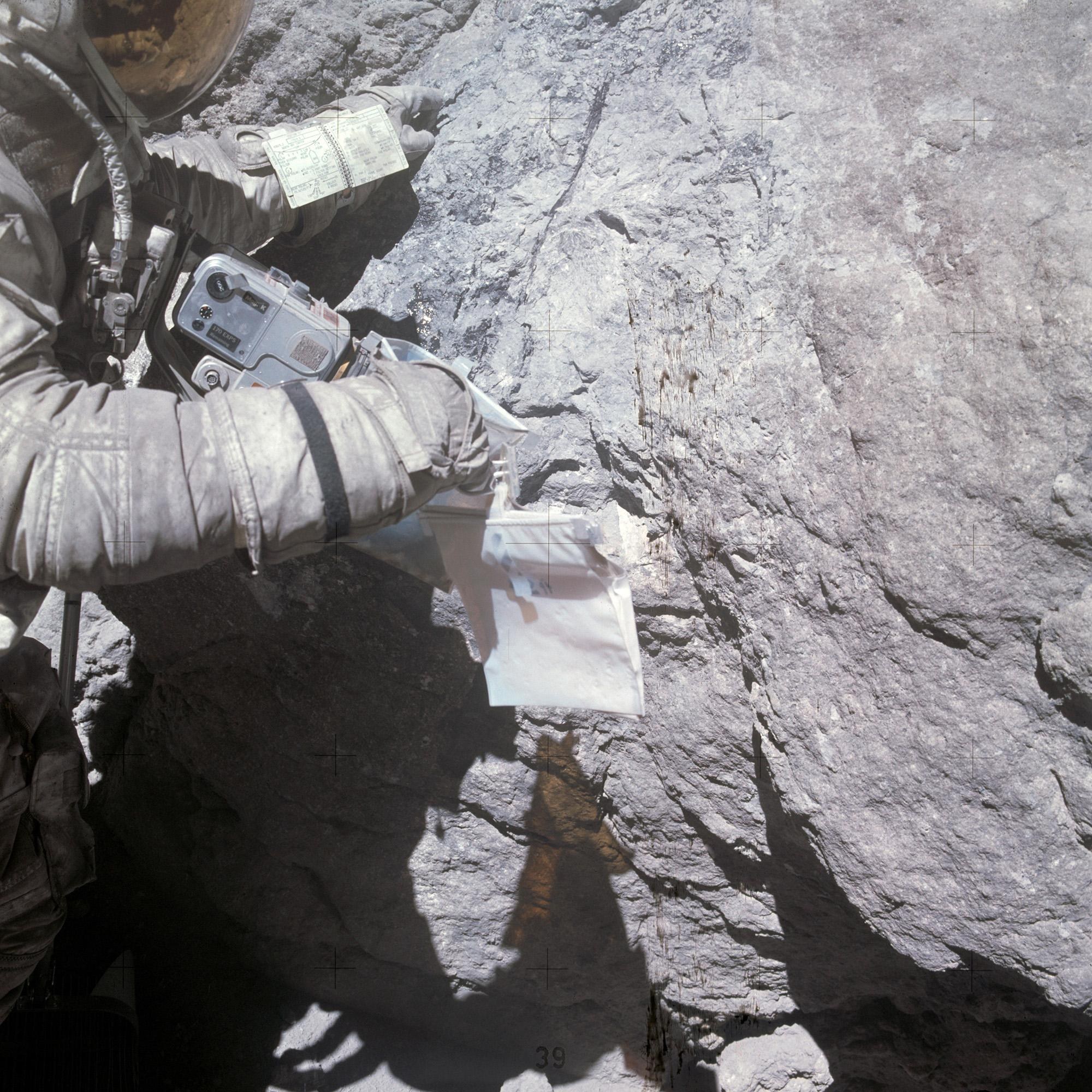 Charles Duke points to a feldspar crystal on Houston Rock; the excursion manual can be seen on his left arm