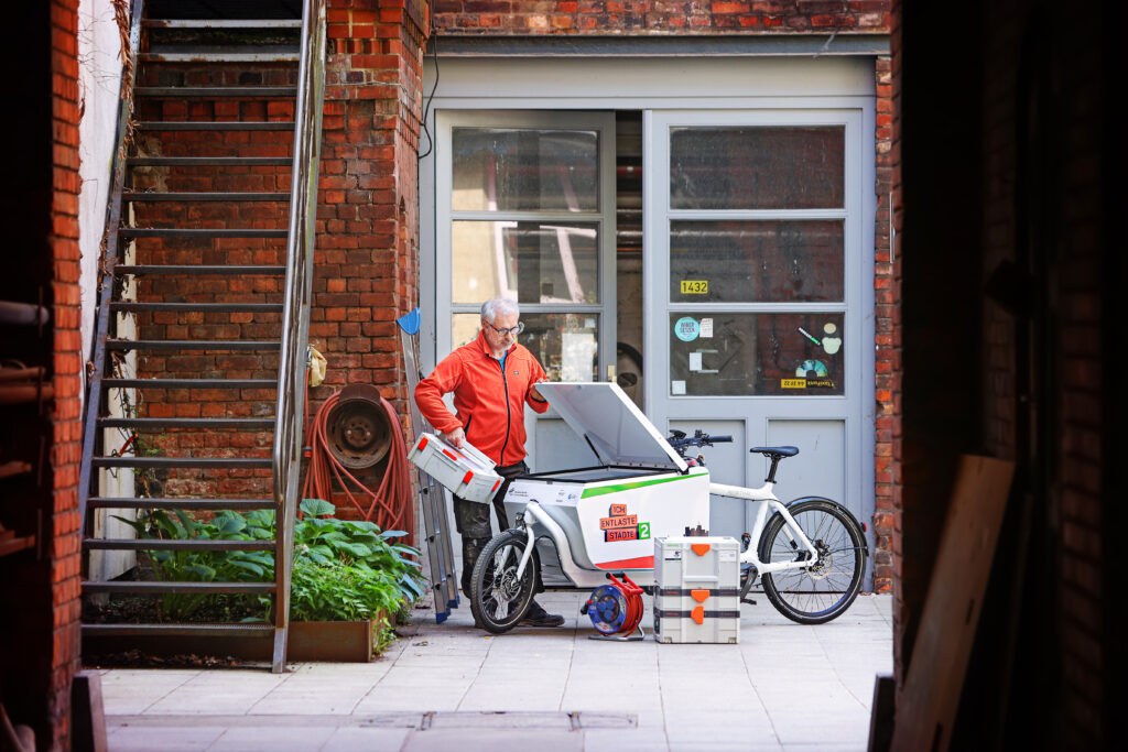 In a backyard, a man in a red jacket loads a cargo bike.