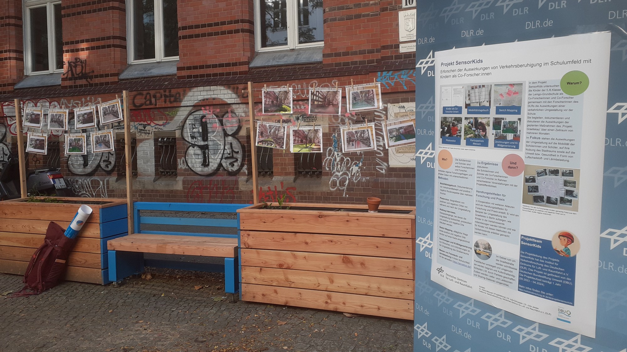 In one of the converted parking bays images of potential further transformations of the Graefekiez are displayed. They are hanging above the wooden structure's planters. A poster explains the SensorKids project in detail.