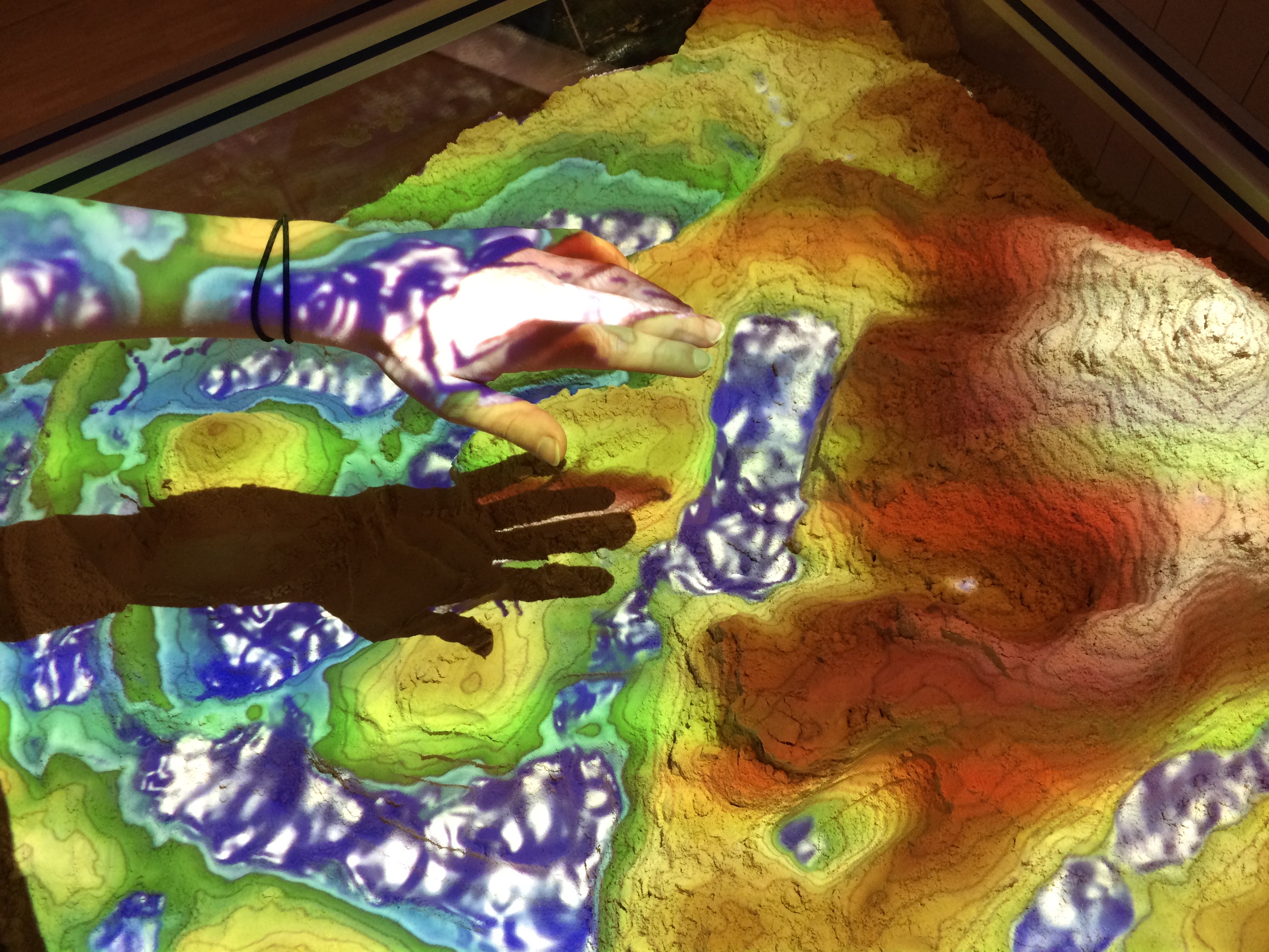 In der virtuellen Sandbox kann man eine Landschaft aus echtem Sand modellieren – und darauf wird dann per Rechner in Echtzeit ein farbiges Höhenmodell projiziert. Bild: DLR