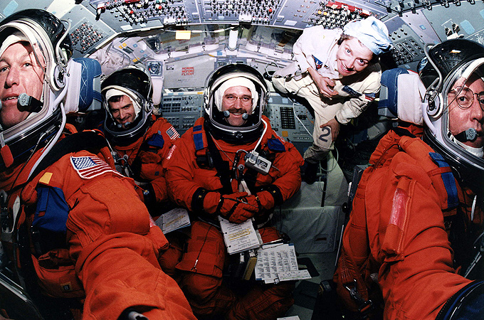 Ein Bild mit Seltenheitswert: Hier sieht man eine Shuttle-Crew kurz vor dem Start. Die Raumfähre ist senkrecht an der Startrampe aufgerichtet, so dass die Astronauten mit dem Rücken zum Boden in ihren Sitzen liegen. Die Technikerin, die hinten rechts zu sehen ist, steht auf der Wand … 
Bild: NASA